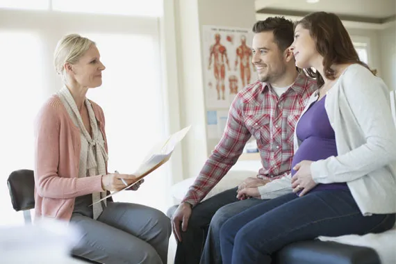  Une médecin souriante s'adresse à un couple de femmes enceintes dans une salle d'examen.